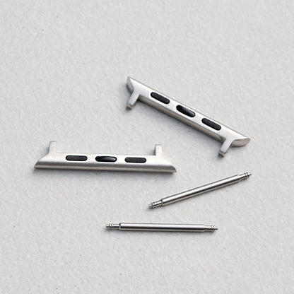 A set of silver metal watch strap adapters arranged on a light gray textured background.