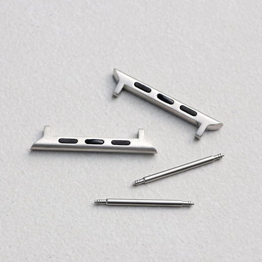A set of silver metal watch strap adapters arranged on a light gray textured background.