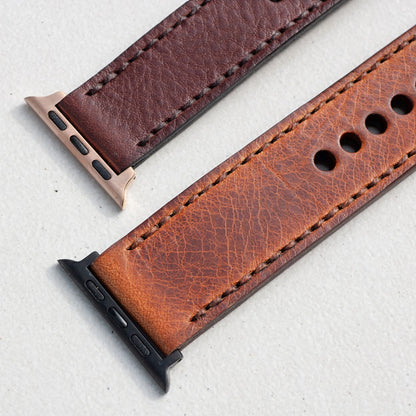 Two leather watch straps with textured grain, one in dark brown and one in warm cognac brown, shown with metal and black watch connectors on a light gray background.