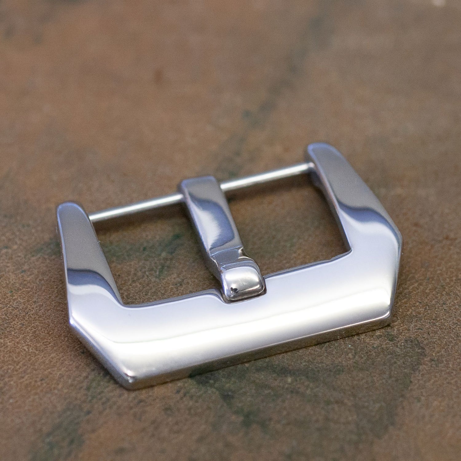 A polished silver metal watch buckle resting on a textured brown leather surface.