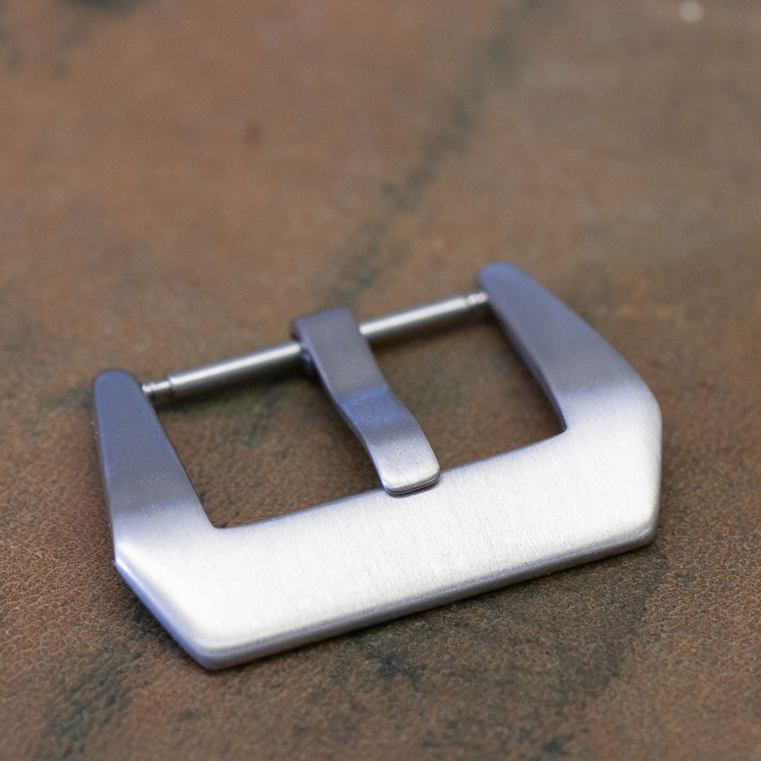A brushed silver metal watch buckle with a matching metal loop, resting on a textured brown surface.