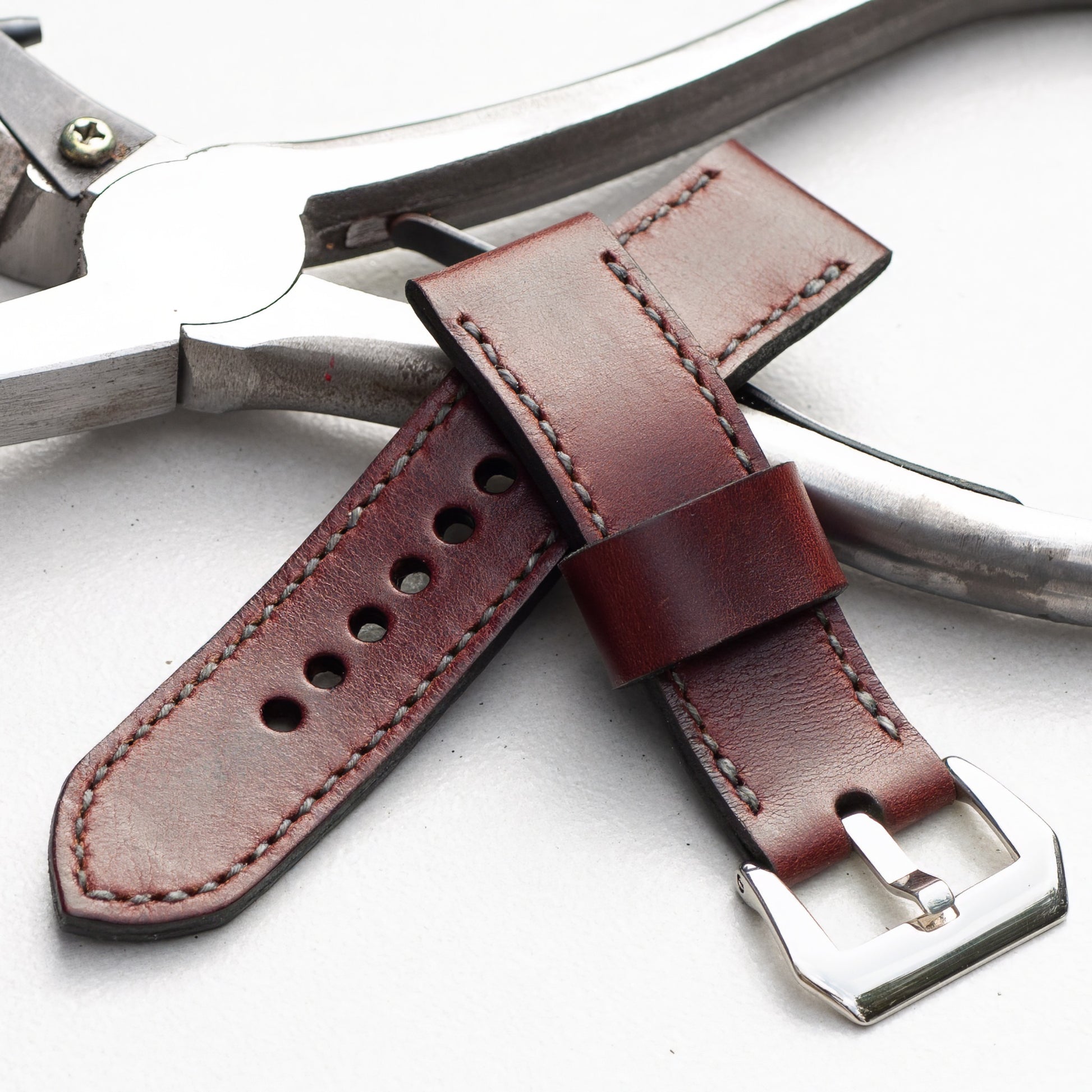 Burgundy leather watch strap with grey stitching and polished steel buckle
