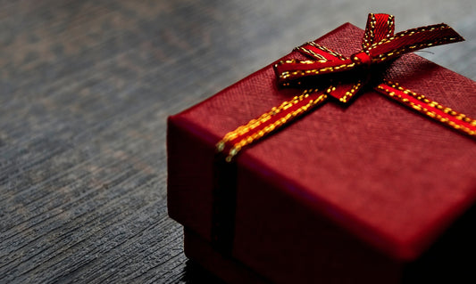 A red gift box wrapped with a red ribbon featuring gold trim, tied in a bow, set on a dark wooden surface.