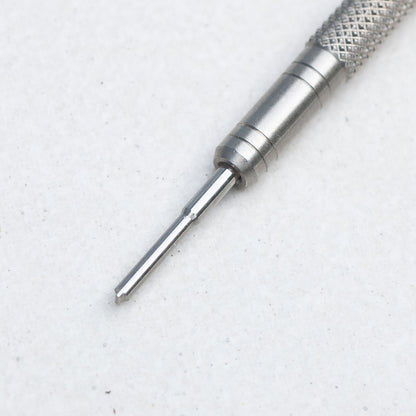 A close-up of a silver metal precision screwdriver bit with a knurled textured handle, shown on a light gray textured background.