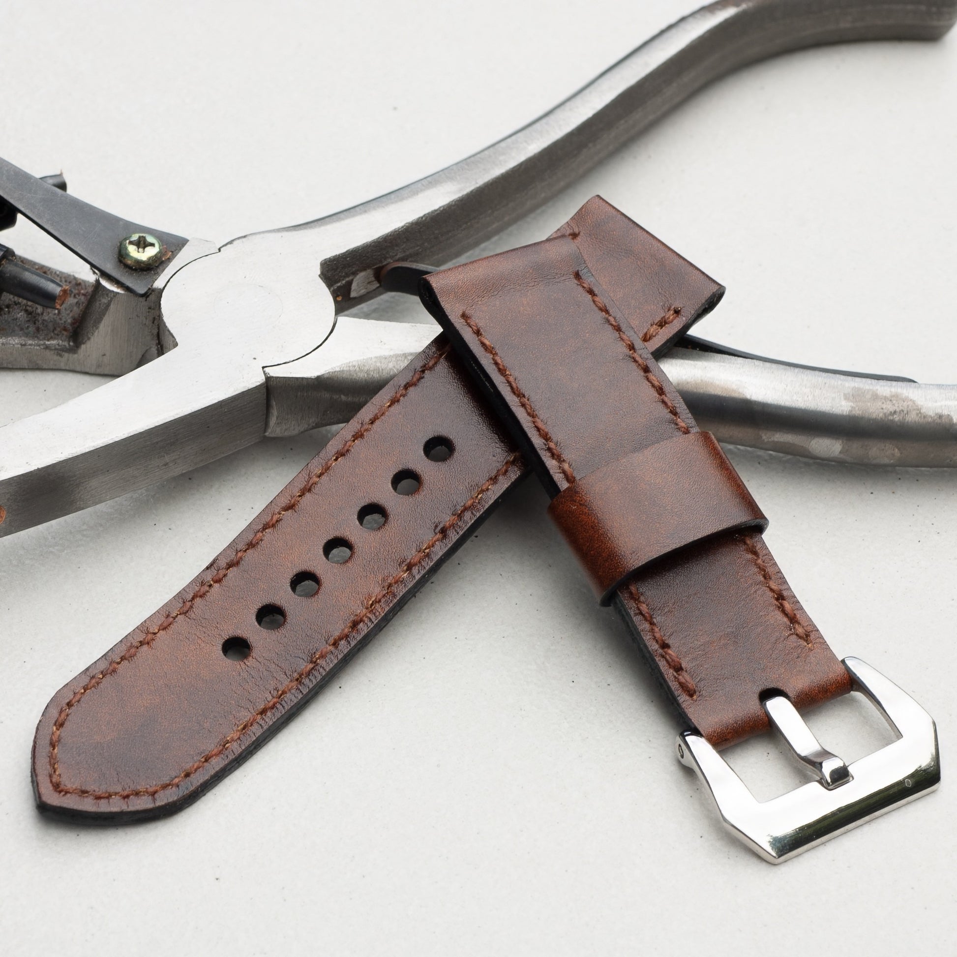 Mahogany leather watch strap with light brown stitching and polished steel buckle