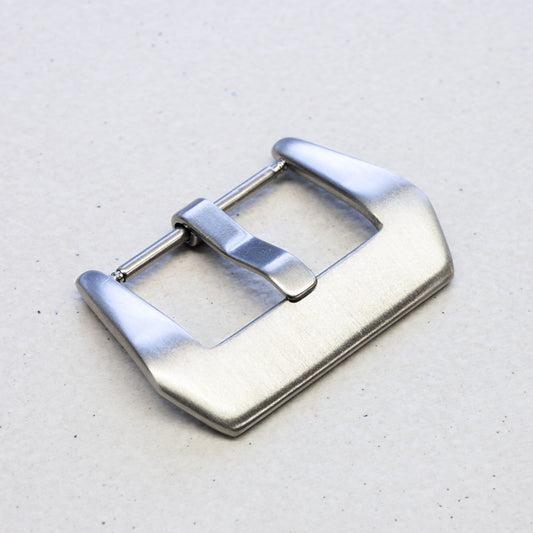 A brushed stainless steel watch strap buckle with a polished pin, shown on a light textured gray background.