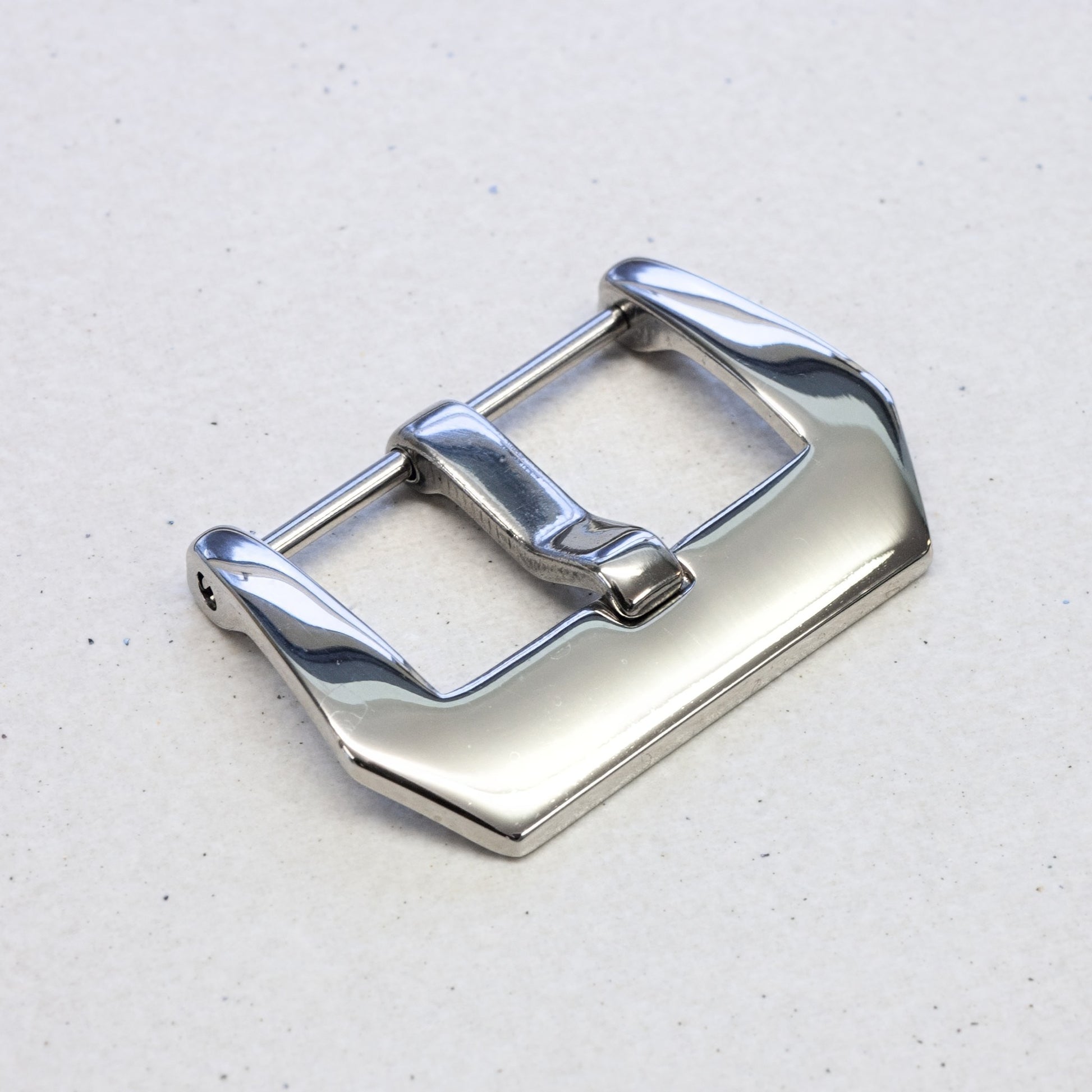 A polished silver metal watch strap buckle, shown at an angle on a light gray textured background.