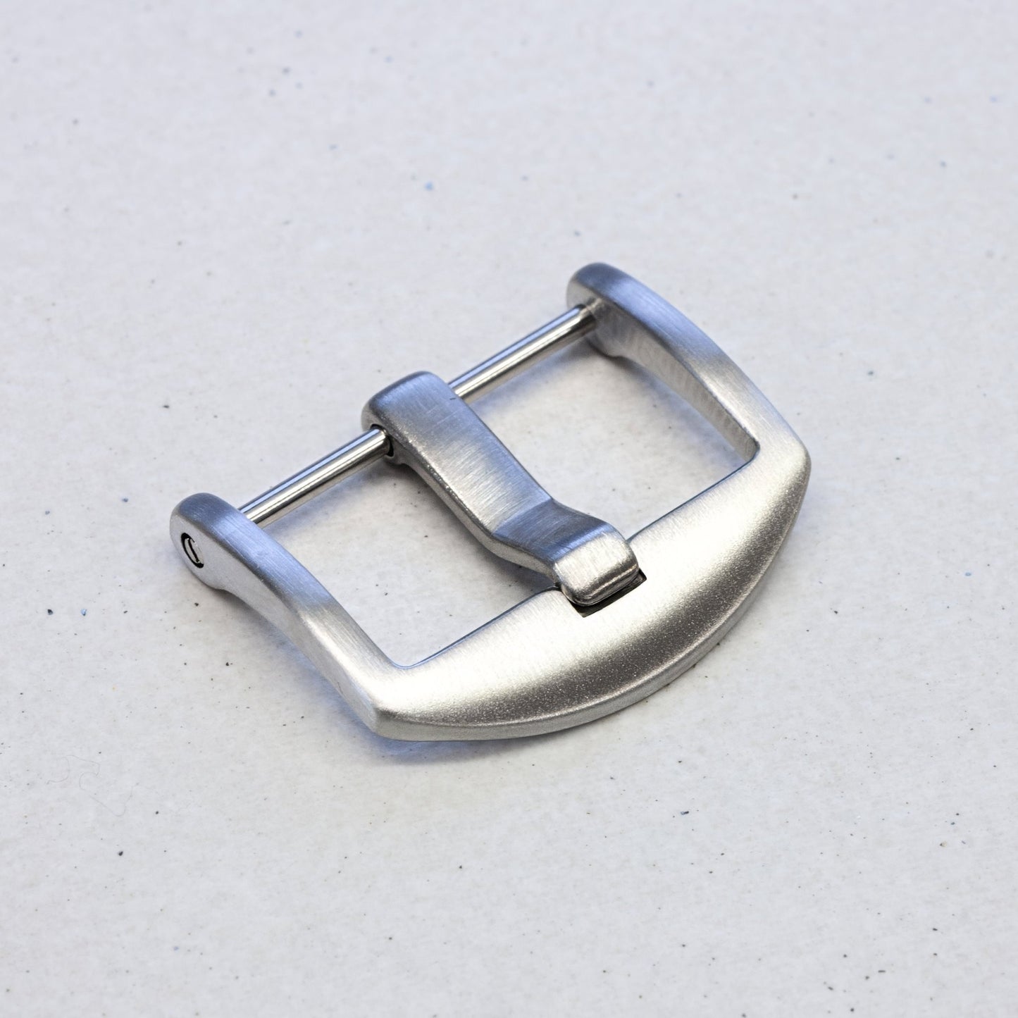 A silver stainless steel watch strap buckle with a brushed finish and a curved guard, shown on a light gray textured background.