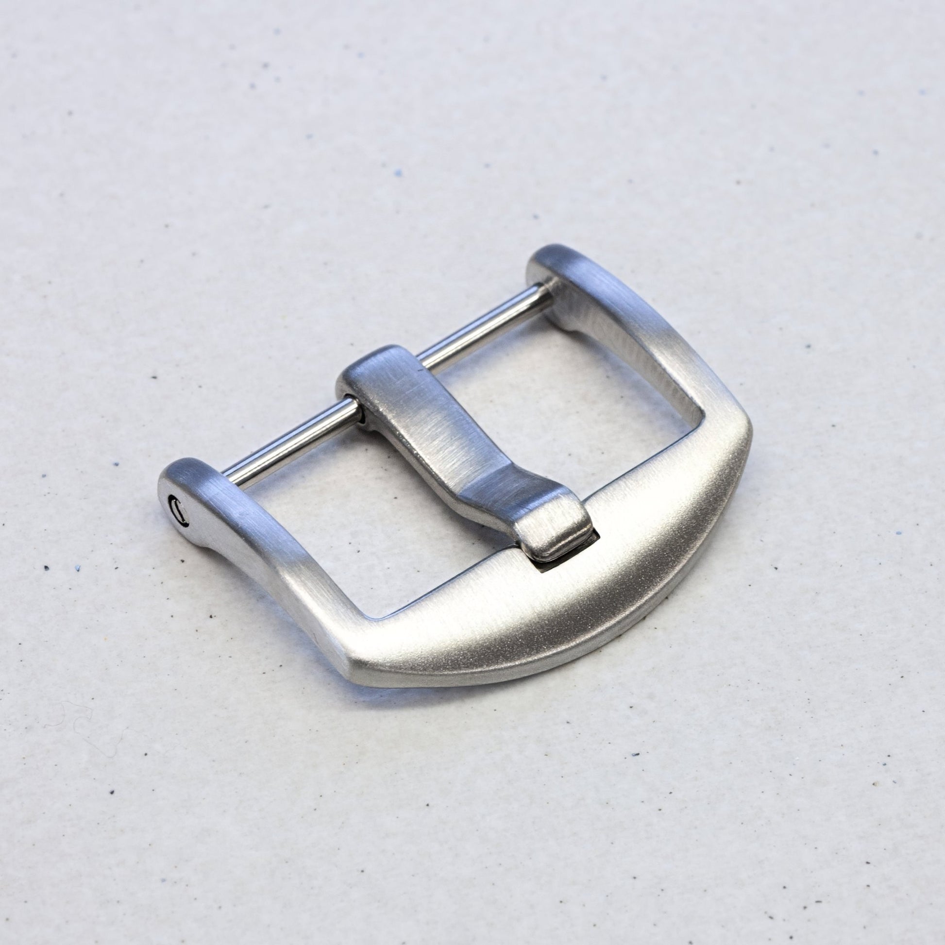 A silver stainless steel watch strap buckle with a brushed finish and a curved guard, shown on a light gray textured background.