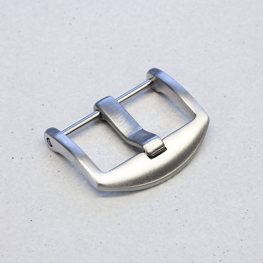 A silver stainless steel watch strap buckle with a brushed finish and a curved guard, shown on a light gray textured background.