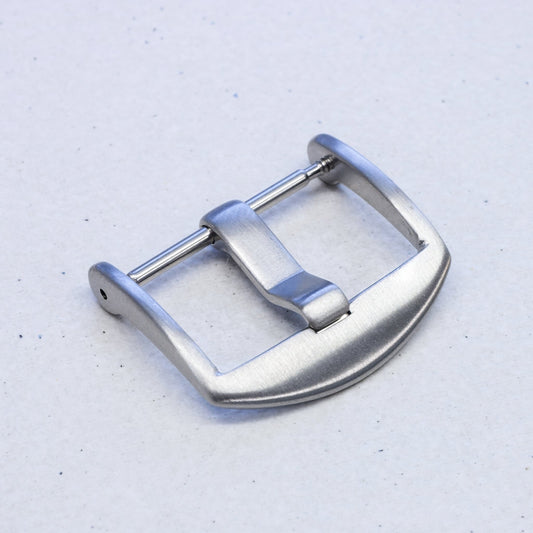 A brushed silver metal watch strap buckle, shown from a top-down angle on a light gray textured background.