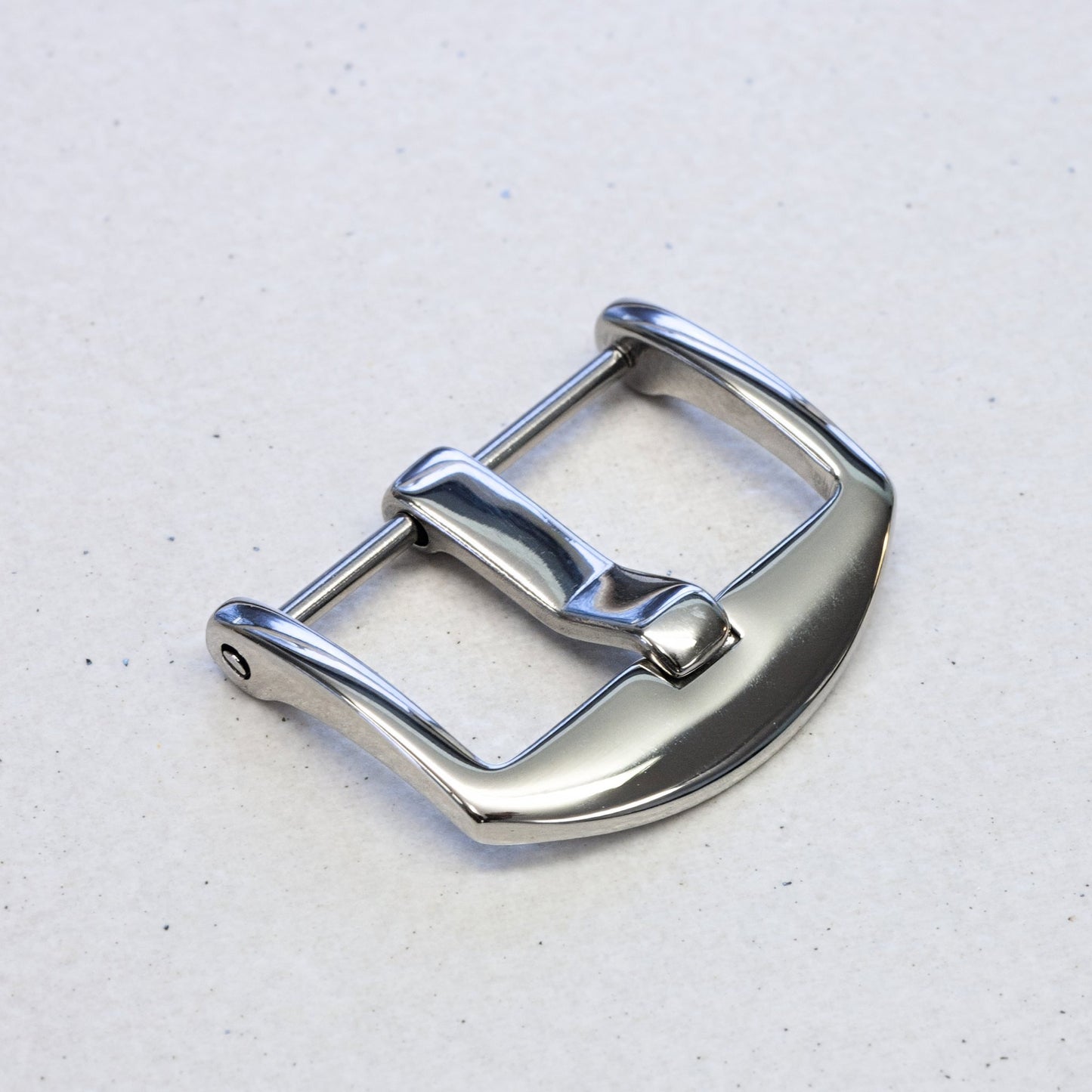 A polished stainless steel watch strap buckle with a curved profile, shown on a light gray textured background.