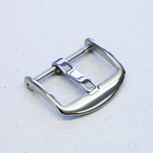 A polished silver stainless steel watch strap buckle, photographed on a light gray textured background.