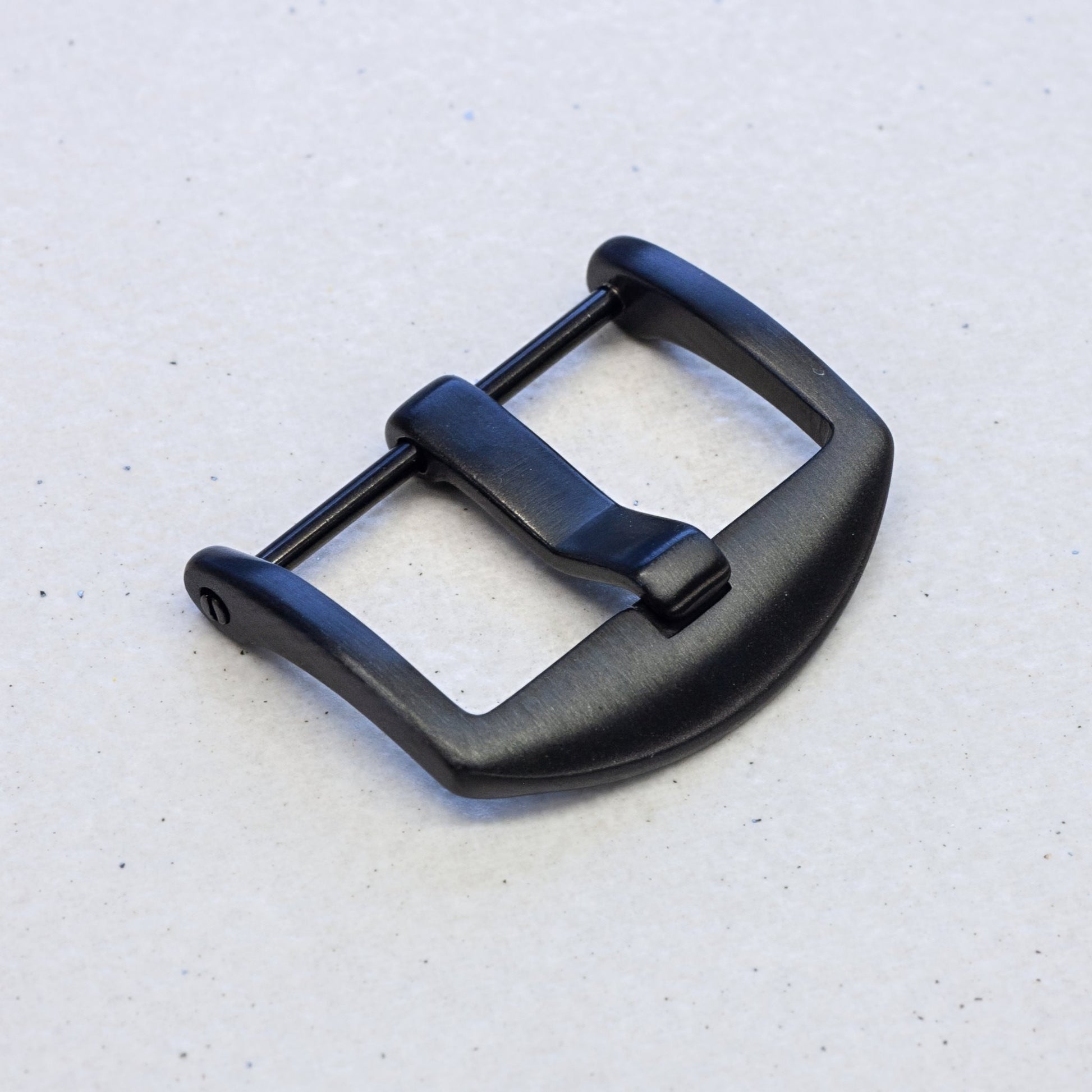 A matte black metal watch buckle with a curved D-shaped profile, shown on a light gray textured background.