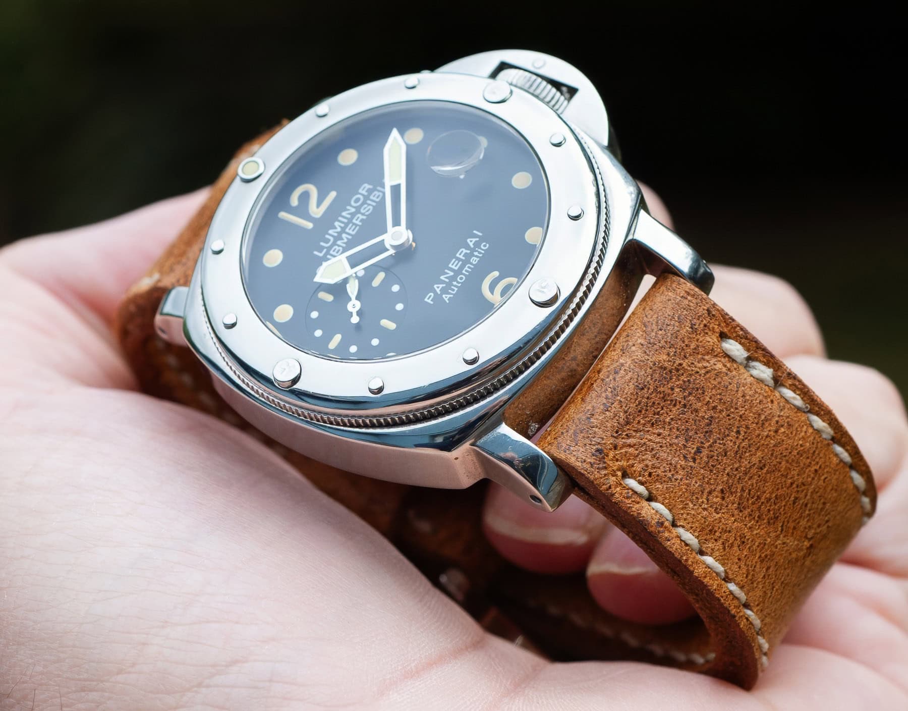 Panerai Luminor Submersible watch held in hand, fitted with a handmade Bruiser leather strap showing rugged grain, warm brown tone, and contrast stitching.